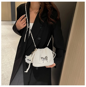 Close-up of a white drawstring bucket bag with silver butterfly buckle and plush ball