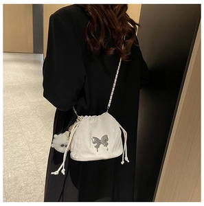 Detail of white bucket bag with silver butterfly charm and chain strap against a black suit