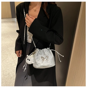 Silver metallic drawstring bucket bag with chain strap and cute plush charm on model
