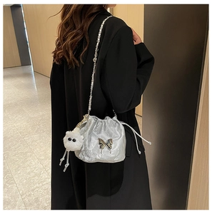 Detail of silver drawstring bucket bag with metallic butterfly logo and plush charm