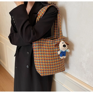 Detail der bunten Hahnentritt-Tasche mit süßem Welpen-Plüsch-Anhänger auf schwarzem Mantel