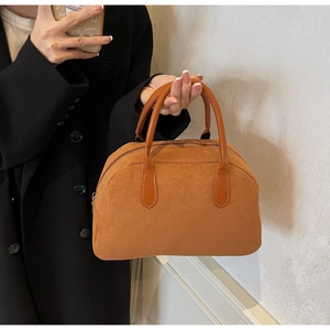 Brown suede Boston handbag shown held by a model wearing a black blazer for styling