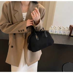 Close-up of black suede Boston bag held by model wearing a khaki double-breasted blazer