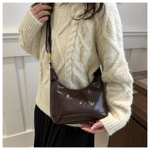 Detail of a dark brown glossy hobo bag with embossed maison logo and gold buckle