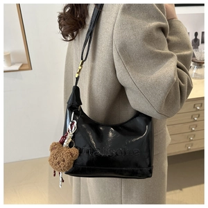 Detail of black glossy underarm bag with embossed text and a cute brown plush bear charm