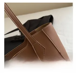 Detailed close-up of brown leather tote bag with white contrast stitching and reinforced handle