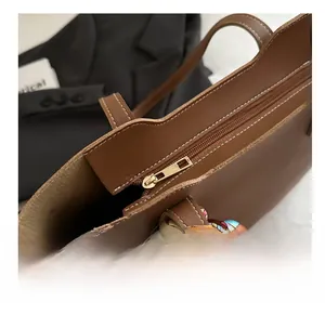 Macro detail of brown tote bag featuring golden zipper and decorative silk scarf handles
