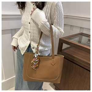 Detail of a brown leather tote bag with white contrast stitching and a silk scarf handle