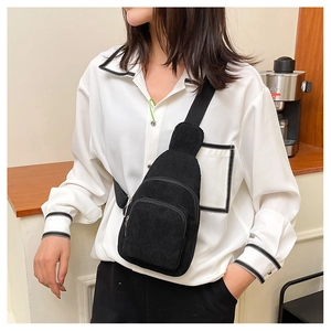 Close-up of black corduroy chest bag with multiple zippers and adjustable strap worn by model
