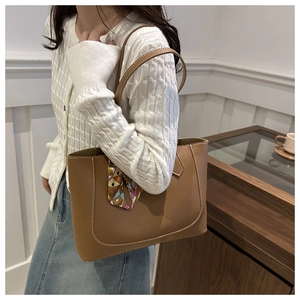 Close-up of brown leather tote bag featuring contrast stitching and silk scarf on handle