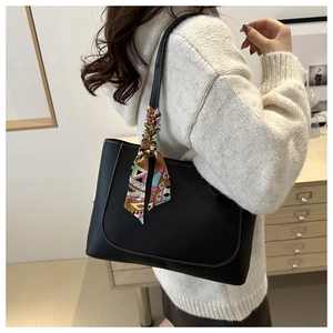 Detail of black leather tote bag with white stitching and colorful silk scarf on handle