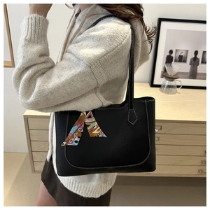 Black leather tote bag with white stitching and decorative silk scarf in a lifestyle setting