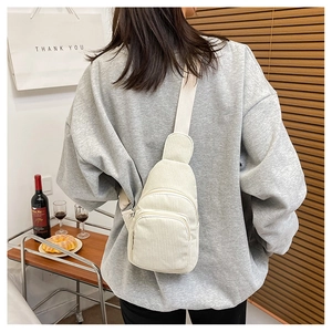 Detail of off-white corduroy chest bag featuring textured fabric and dual zipper pockets