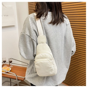 Detailed back view of a cream corduroy crossbody bag worn on a model in a cozy interior