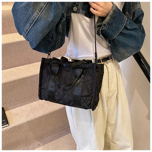 Close-up of black quilted nylon tote bag worn cross-body style with casual denim outfit