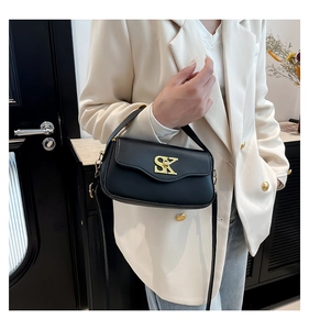 Schwarze Umhängetasche mit goldenem SK-Logo am Model in weißem Blazer gezeigt