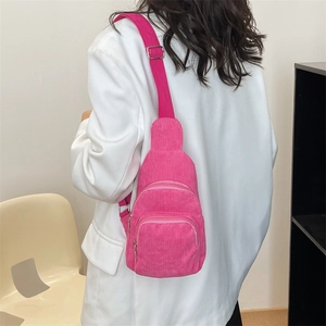 Detail of bright pink corduroy crossbody bag with adjustable strap worn on white blazer