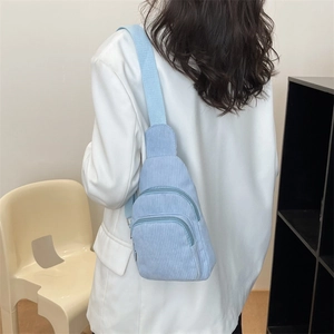 Close-up of a light blue corduroy chest bag worn over a white blazer in a minimal setting