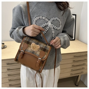 Close-up of retro plaid handbag featuring a plush teddy bear patch and silver buckles