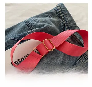 Dettaglio della tracolla larga in nylon magenta con fibbia in metallo dorato su jeans