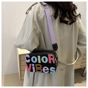 Dettaglio della borsa a tracolla con patchwork di lettere 3D e cinturino viola su modella