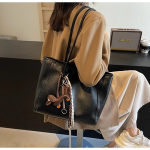 Detail of black leather tote bag featuring a cute dachshund pendant and slim shoulder straps