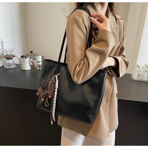 Detail of a large black tote bag with dog charm on a shoulder, minimalist cafe background