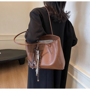 Detailed side view of brown leather tote bag featuring a horse charm and woven tassel