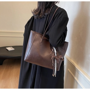 Detail of dark brown leather tote bag with slim straps and a cute dog charm on black coat