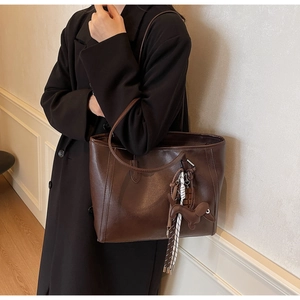 Detail of a large dark brown leather tote bag with a creative dog charm on a model
