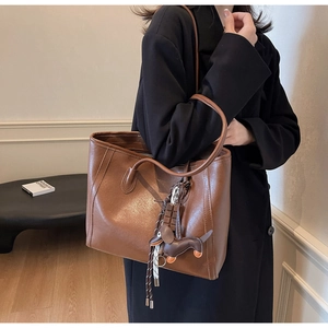 Brown leather tote bag with long straps and dachshund doll charm shown on a model