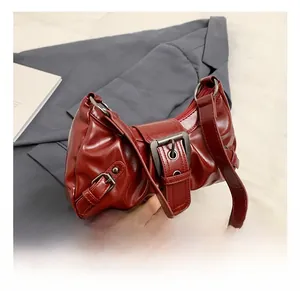 Detail view of burgundy faux leather handbag with metallic buckle and wide shoulder strap