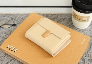 Détail du portefeuille en cuir PU beige avec fermoir doré en cœur sur un carnet brun