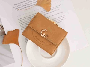 Close-up of frosted brown tri-fold wallet with a golden rabbit buckle on a ceramic plate