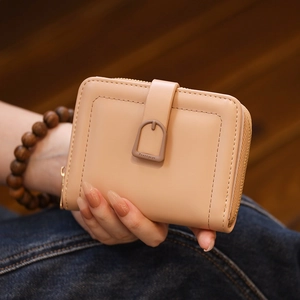 Detail of nude beige PU leather wallet with zipper and buckle held by a model
