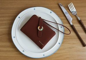 Close-up of a brown textured leather wallet with a golden buckle on a white plate