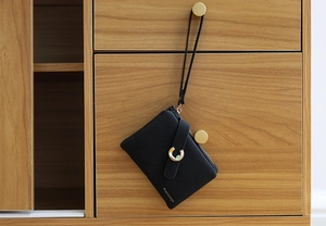 Detail of black textured leather coin purse with golden hardware and hanging strap