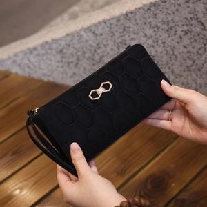 Detail of black long wallet featuring hexagonal quilted texture and golden bow hardware