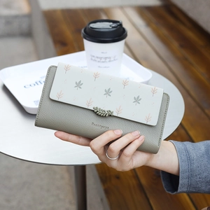 Gros plan du portefeuille long vert olive à motif floral tenu à la main dans un café