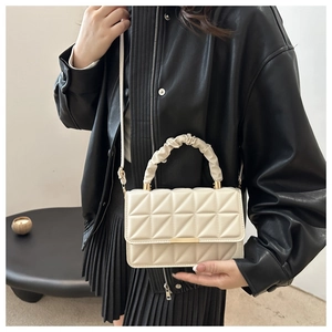 Detail of cream white quilted crossbody bag with textured handle and gold metal clasp