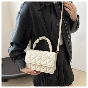 Detail of ivory quilted flap bag featuring a scrunchie handle and gold metal lock clasp