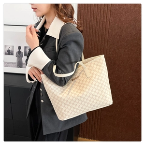 Détail d'un grand sac cabas beige avec imprimé M et plaque en métal porté à l'épaule