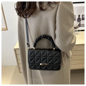 Detail of black quilted crossbody bag with a cloud-style handle and gold metal lock
