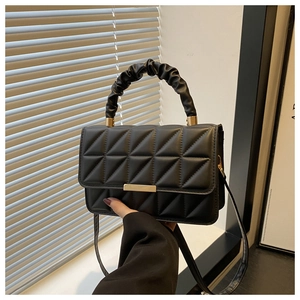Close-up of black quilted PU leather handbag with golden lock and ruched handle detail