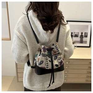 Detail of floral woven bucket backpack with leather base and drawstring on white sweater