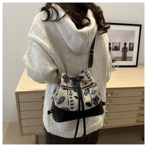 Ethnic woven drawstring bucket bag with floral patterns and black leather straps