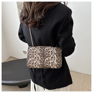 Détail du sac léopard à chaîne avec bordure dorée porté sur une veste de blazer