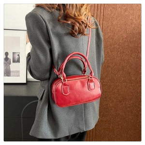 Polished red leather boston bag with top handles and adjustable shoulder strap worn by model