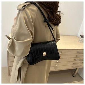 Detail view of black crocodile pattern shoulder bag with golden buckle on khaki trench coat
