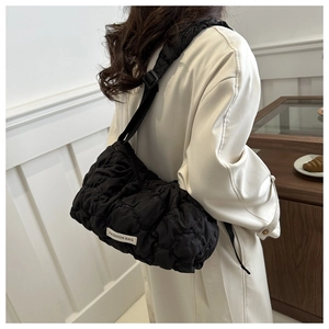 Close-up of black quilted puff shoulder bag with adjustable strap and side logo tag